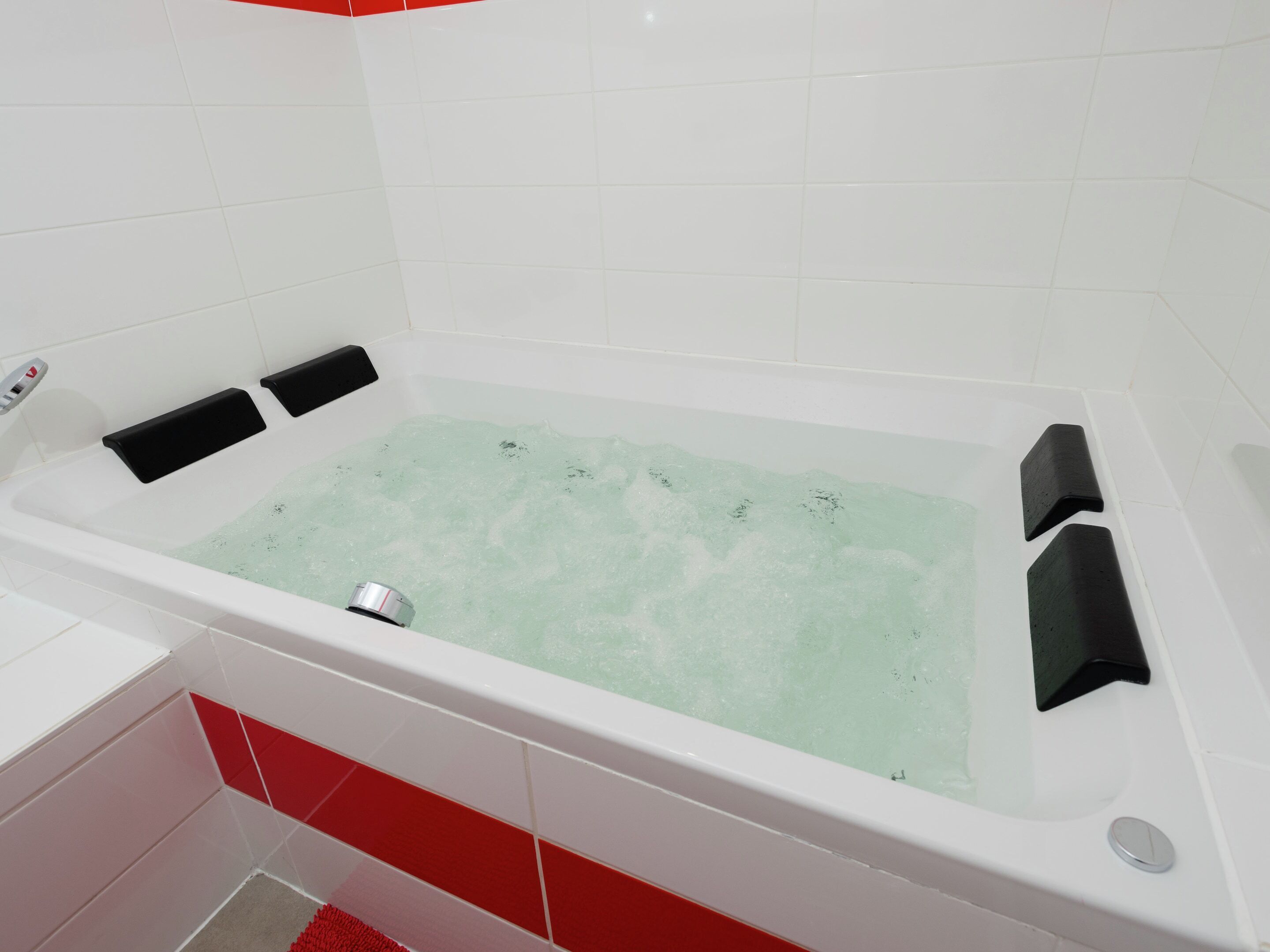 Une salle de bain moderne avec une baignoire blanche, des touches de rouge et un chauffe-eau apparent.