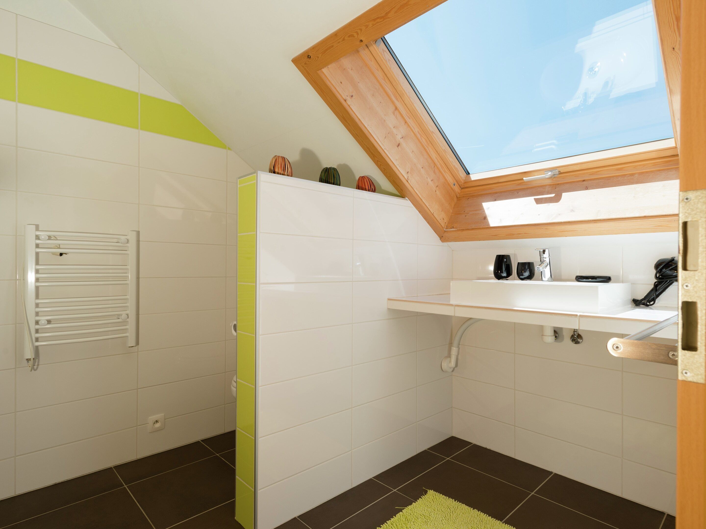 A modern bathroom with a skylight, white tiles, a towel rack, a sink with a mirror, and a green rug.