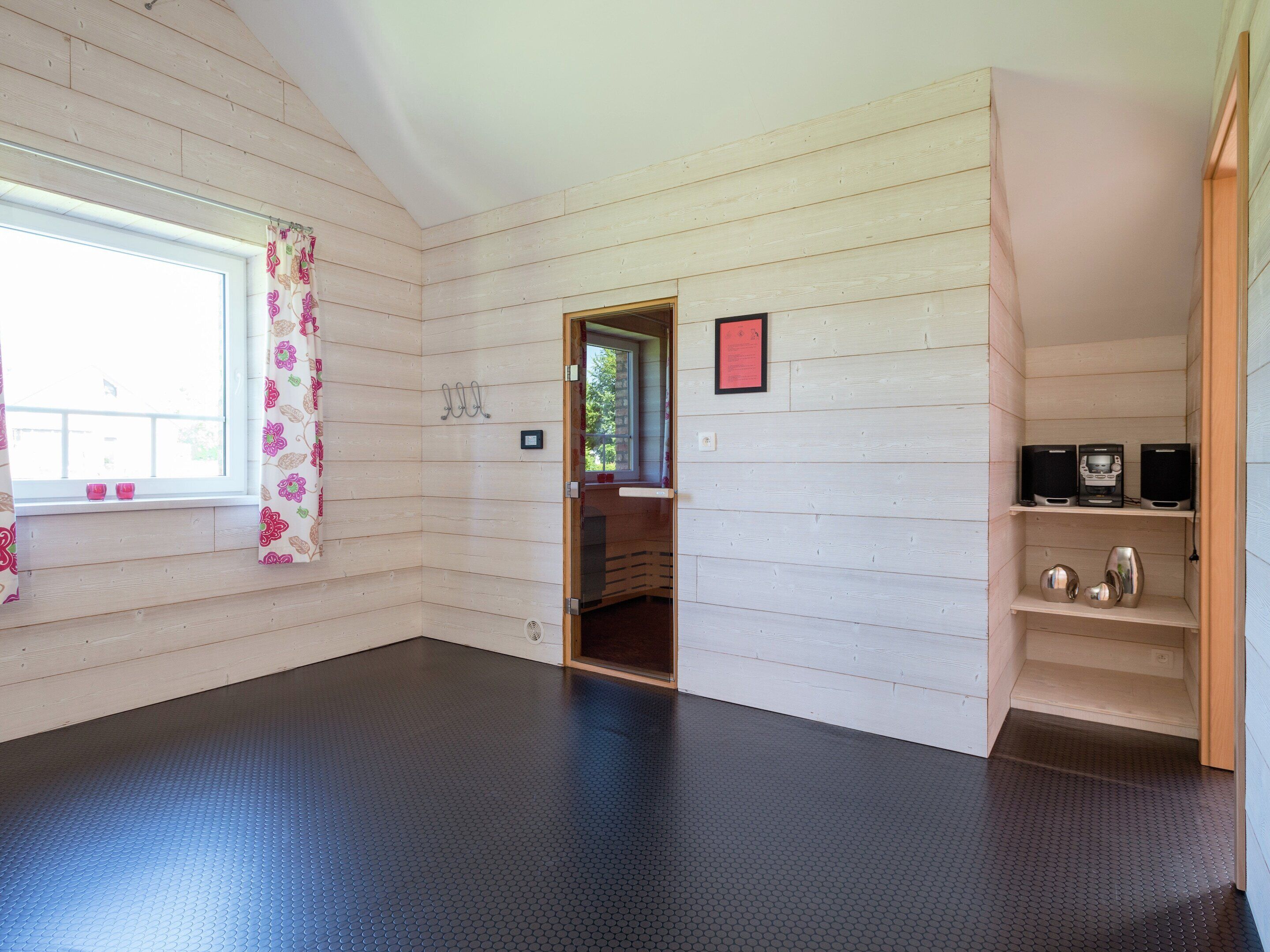 Ein Zimmer mit holzverkleideten Wänden, dunklem Boden und einem Fenster mit blumigen Vorhängen.