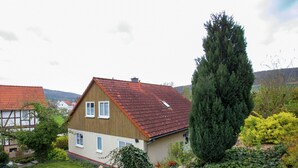 A house with a sloped roof, a garden with a large tree, and a view of other houses in the background. - Ferienhaus in Homberg (Homberg)
