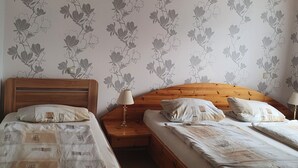A room with two wooden beds, each with a headboard, a nightstand, and a lamp. The walls have a floral wallpaper pattern. - Ferienhaus in Homberg (Homberg)