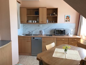 A compact kitchen with a dishwasher, a toaster, and a coffee maker. There is a dining table with a placemat and a vase of flowers.
