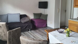 A small, cozy living area with a sofa, a small table with a floral tablecloth, and a television mounted on the wall. - Ferienhaus in Homberg (Homberg)