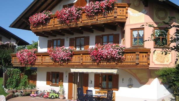 Un chalet traditionnel doté de balcons en bois, d’un patio couvert et d’un jardin avec des jouets et une tondeuse à gazon.
