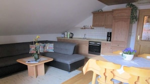 Un espace de vie compact comprenant un canapé, une petite table, une table à manger avec des chaises, un coin cuisine avec des placards et des appareils électroménagers, et une fenêtre donnant sur un paysage agréable.