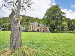 Un grand bâtiment historique en briques, doté de nombreuses fenêtres et d’une entrée imposante, entouré de champs verdoyants et d’arbres.