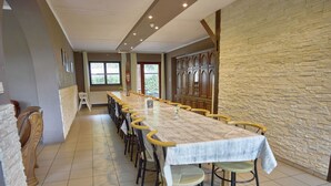 A long dining table with chairs, a stone wall, and a view of greenery outside.