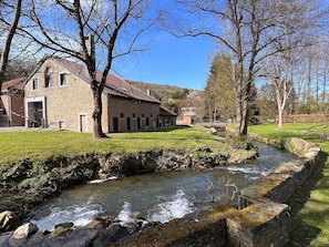A stone building with a red roof, a small stream, and a bridge in the background. - Mansion With Pool, Neblon (Ouffet)