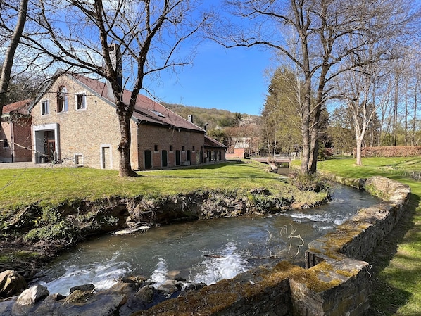 Un bâtiment en pierre avec un toit rouge, un petit ruisseau et un pont en arrière-plan.