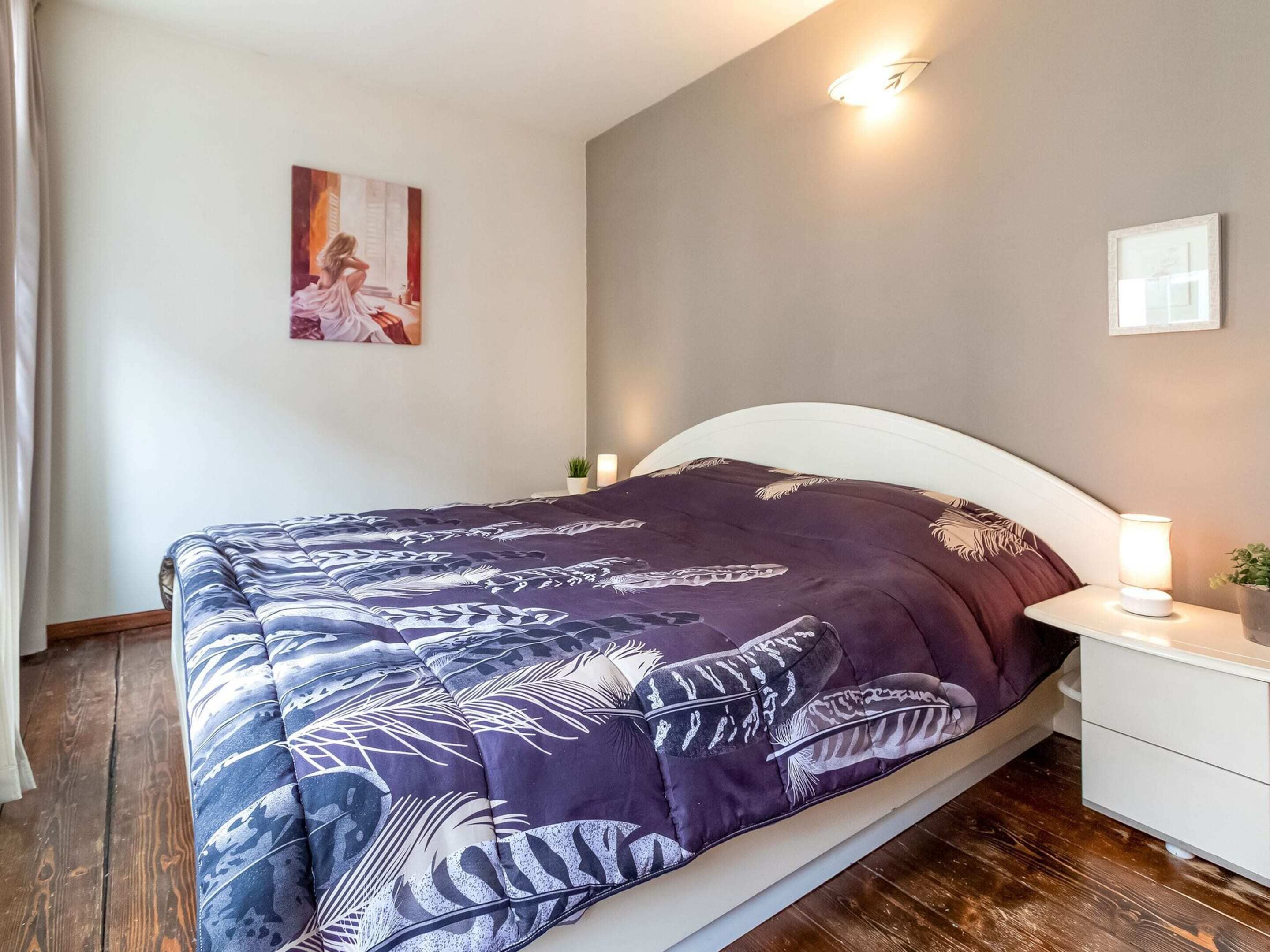 Une chambre à coucher comprenant un lit, des tables de chevet, une petite table, une lampe fixée au mur et un tableau encadré.
