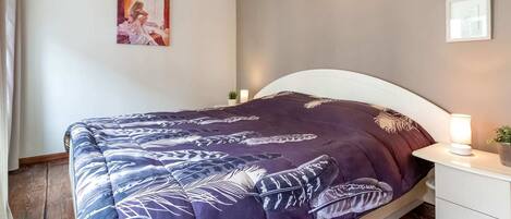 Une chambre à coucher comprenant un lit, des tables de chevet, une petite table, une lampe fixée au mur et un tableau encadré.