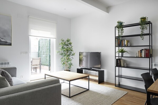 A modern living room with a sofa, coffee table, TV, bookshelf, and potted plants.