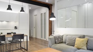 Un salon moderne avec un canapé gris, une table basse en bois et des chaises noires. On y trouve également un coin repas avec une table et des chaises en bois.