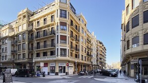 Un immeuble à plusieurs étages doté de balcons, avec un magasin au rez-de-chaussée et des voitures garées.