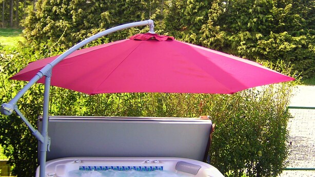 A hot tub with a pink umbrella, surrounded by greenery.