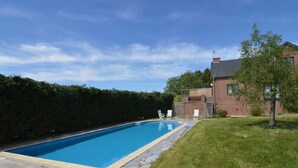 A rectangular swimming pool with stone edging, surrounded by a grassy lawn and a hedge.
