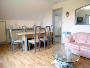 A dining area with a table and chairs, a pink sofa, and a glass coffee table with decorative items.