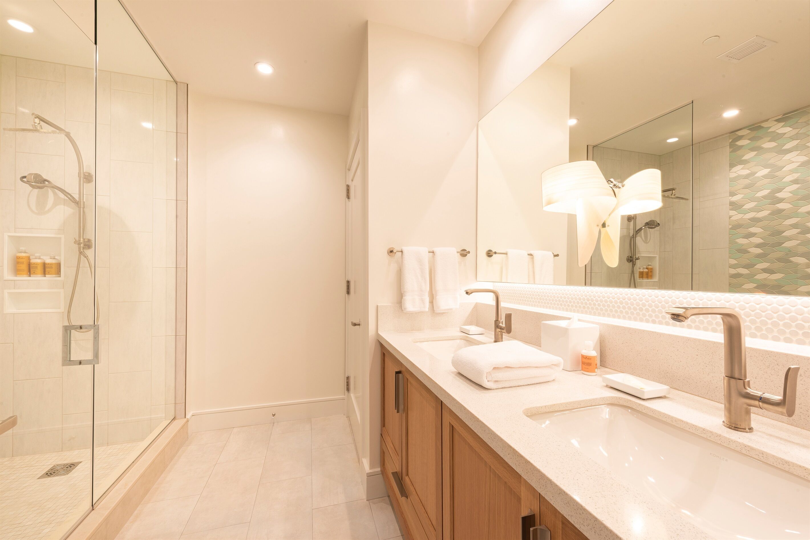 Un baño moderno con ducha envuelta en vidrio, un tocador espacioso con espejo y un lavabo.