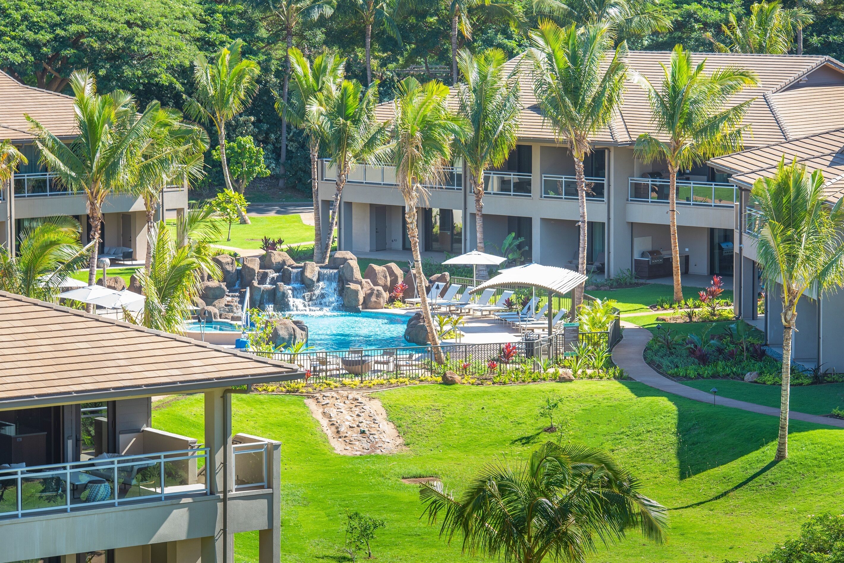 A resort with a swimming pool, palm trees, and a waterfall feature.