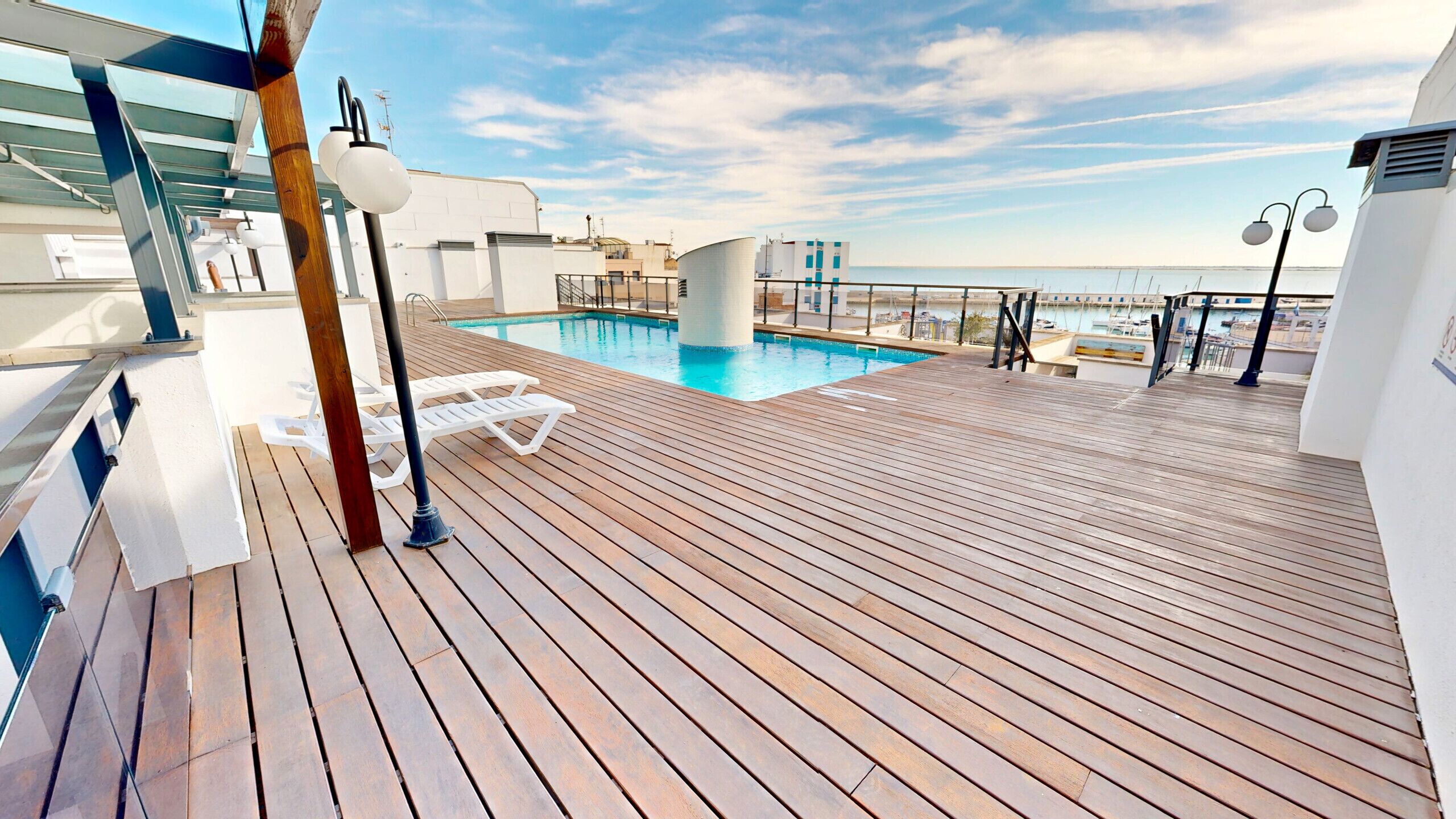 A wooden deck with a pool, lounge chairs, and a view of the sea.