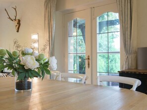 A dining area with a wooden table, white chairs, a vase with white flowers, and a deer skull on the wall. - Mansion in Spa Liege With Private Garden (Spa)