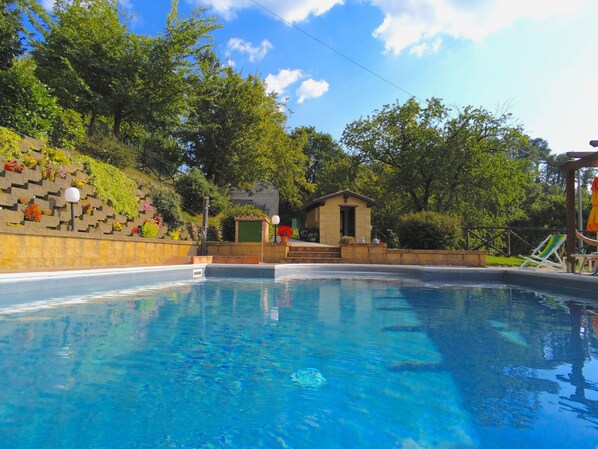 A swimming pool with a stone wall, a small structure, and trees in the background.