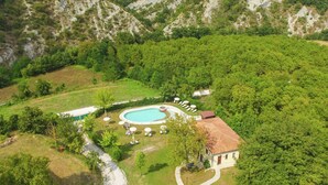 Um resort com piscina, espreguiçadeiras e um pequeno edifício rodeado por vegetação exuberante e colinas.