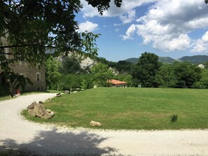 Un paysage rural avec un bâtiment en pierre, une maison à toit rouge et un champ d’herbe.