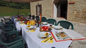 Um espaço de refeições ao ar livre com um edifício de pedra ao fundo, mesa posta com pratos, copos e um livro.
