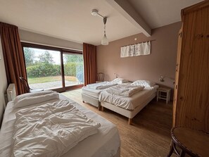 A bedroom with two beds, a wooden floor, a window with curtains, and a ceiling light. - Farmhouse Home in Eede (Eede)