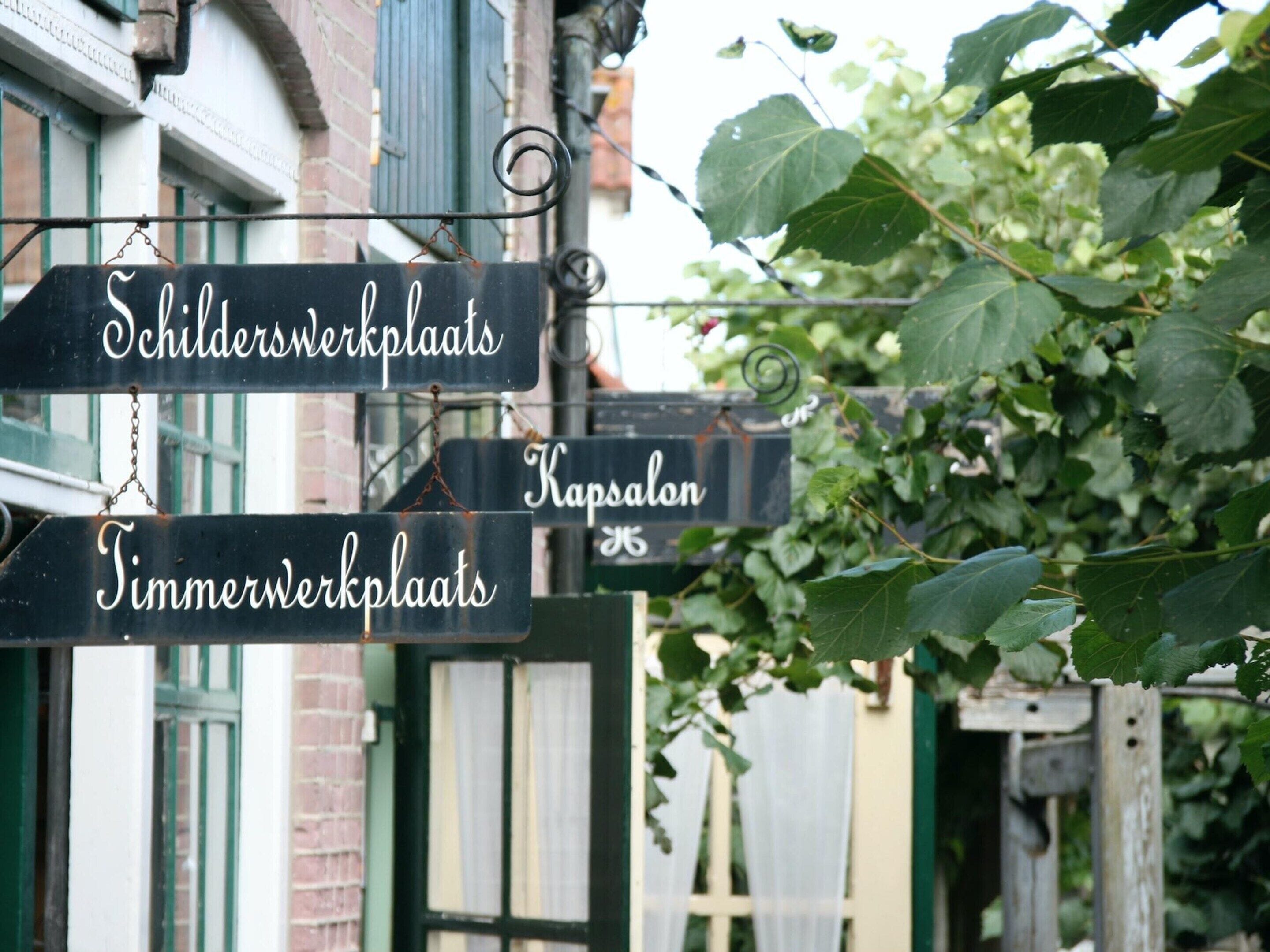 Una señal de calle con indicaciones hacia 'Schilderwerkplaats', 'Kapsalon' y 'Timmerwerkplaats'.