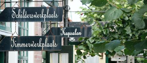 Una señal de calle con indicaciones hacia 'Schilderwerkplaats', 'Kapsalon' y 'Timmerwerkplaats'.