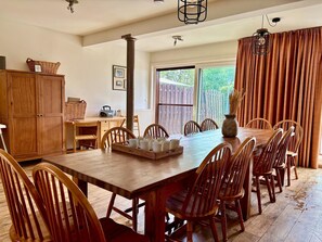 A dining area with a wooden table and chairs, a wooden cabinet, and a window with a view of greenery. - Farmhouse Home in Eede (Eede)