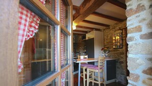 A rustic kitchen with exposed beams, a stone wall, and a wooden table with two chairs. - Forest Hideaway, Baillamont (Bievre)