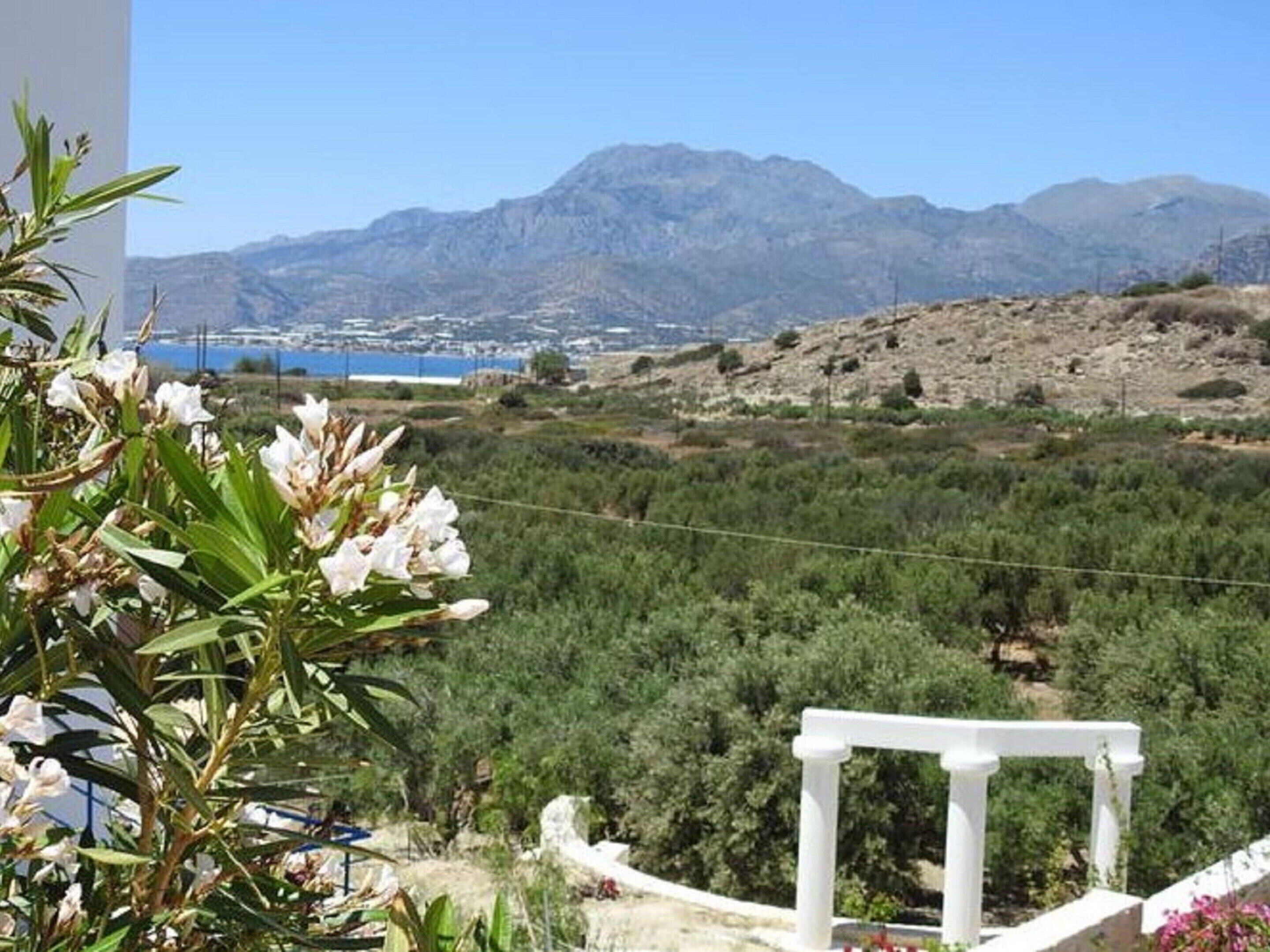 Vista de un paisaje montañoso con una estructura blanca en primer plano, posiblemente un balcón o terraza, con vistas a un valle con vegetación y una masa de agua distante.
