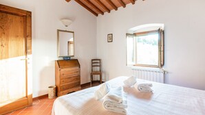 A bedroom with a bed, a wooden dresser, a chair, a window, and a radiator. - Apartment With Swimming Pool in San Casciano (San Casciano in Val di Pesa)