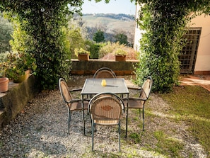 Um pátio com mesa e cadeiras, rodeado por vegetação e vista para colinas.