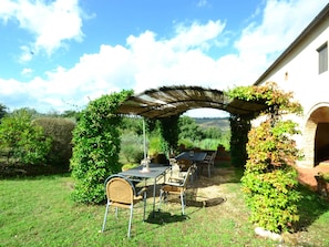 An outdoor patio with a table and chairs, surrounded by greenery and a stone wall.