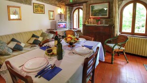 Un coin repas avec une table dressée pour deux personnes, un mur en pierre et un téléviseur en arrière-plan.
