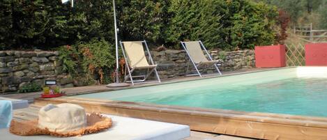 A pool area with lounge chairs, a white umbrella, and a stone wall.