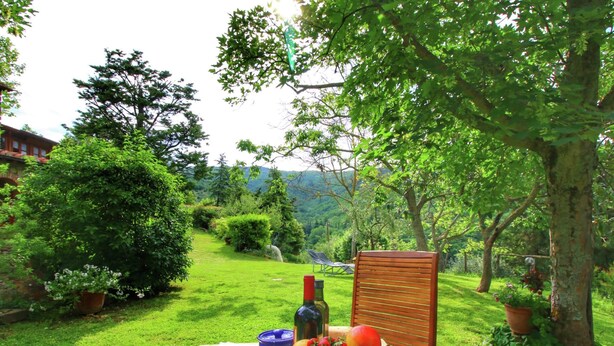 Un coin pique-nique aménagé sur une pelouse, avec une table dressée pour le repas, comprenant des fruits, du pain et une bouteille de vin.