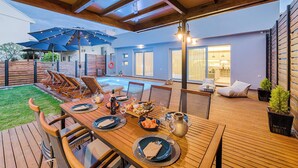 An outdoor dining area with a pool, wooden deck, and a covered seating area. - Nastazia Luxury Beach House (Ialisos)