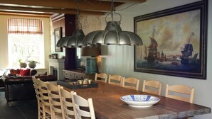 Comedor con mesa de madera, sillas, un cuadro grande y lámparas colgantes.