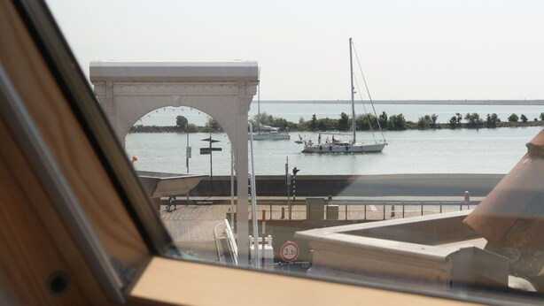 Vista desde una ventana con vista a un puerto deportivo con barcos, una estructura en arco blanca y un puente distante.