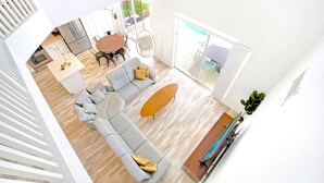 Ein modernes Wohnzimmer mit grauem Sofa, Couchtisch aus Holz und einem Essbereich mit rundem Tisch und Stühlen.