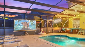 Ein Poolbereich mit einer großen Leinwand, die eine tropische Szene zeigt, Liegestühlen und einem kleinen aufblasbaren Pool.