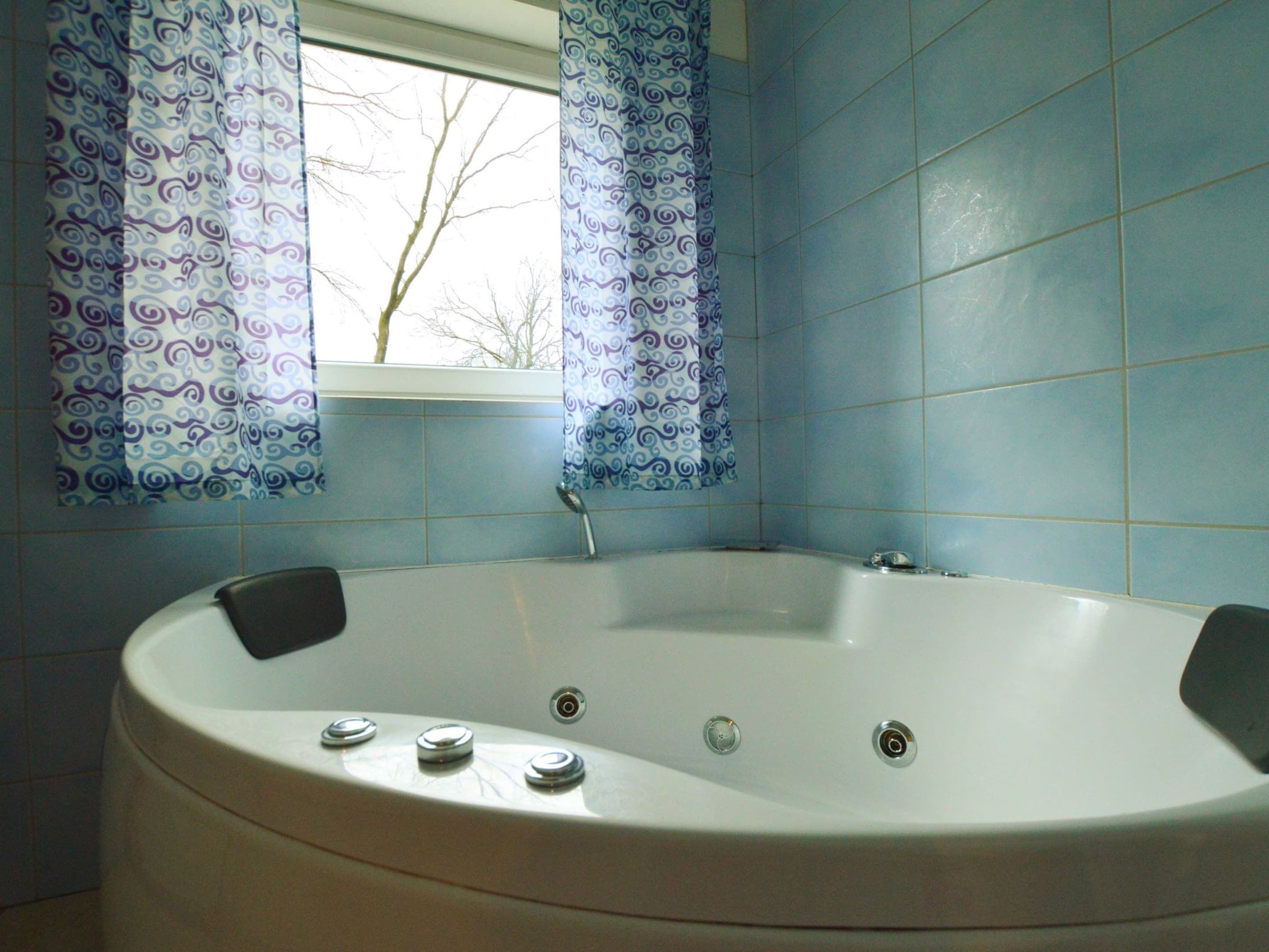 Um banheiro com banheira de pedestal, paredes com azulejos azuis e cortinas estampadas.