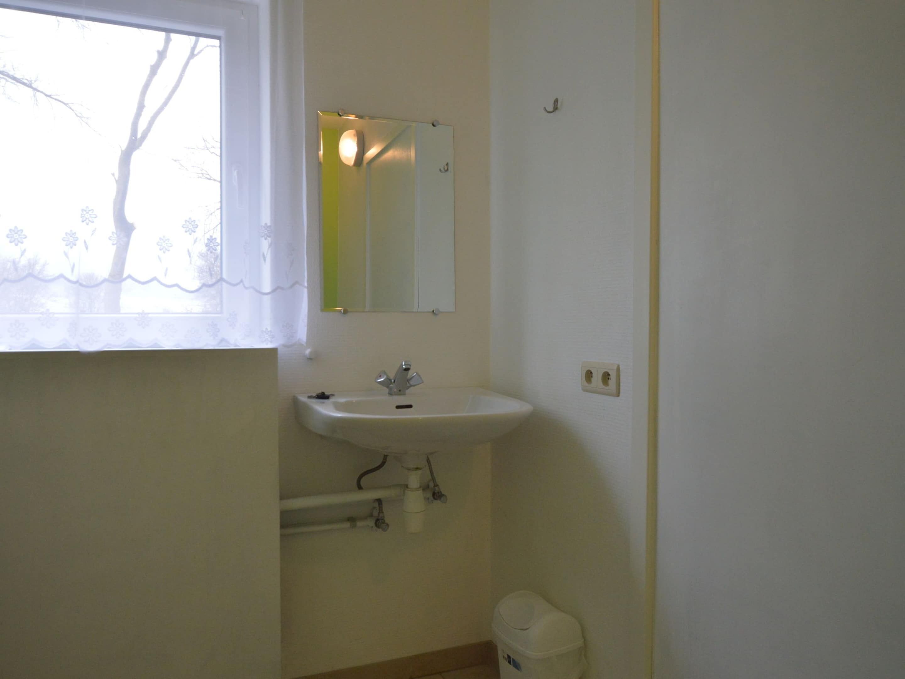 Ein kleines Badezimmer mit Waschbecken, Spiegel und Fenster.