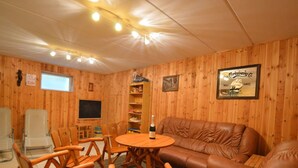 A cozy room with wooden walls, a leather sofa, wooden chairs, a small round table, a television, and a bookshelf. - Holiday Home in Robertville Near Lake & Sauna (Waimes)
