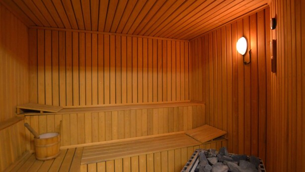 A sauna with wooden walls and benches, a bucket, and a container of rocks. - Holiday Home in Robertville Near Lake & Sauna (Waimes)